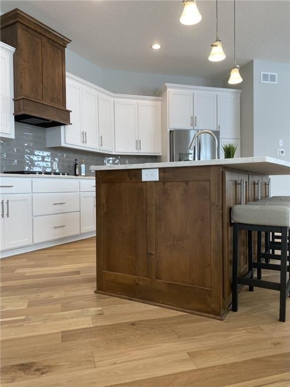 kitchen with a center island with sink, custom range hood, visible vents, hanging light fixtures, and a kitchen breakfast bar