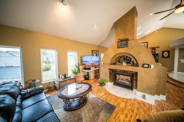 living room with a tile fireplace, ceiling fan, light hardwood / wood-style floors, and vaulted ceiling