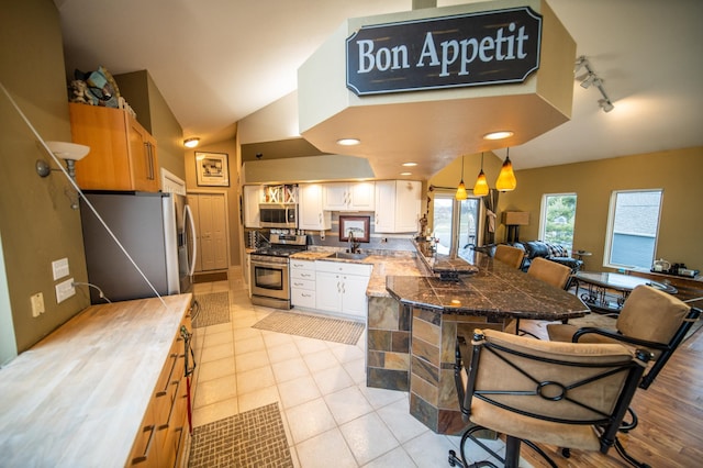 kitchen featuring a breakfast bar, sink, rail lighting, appliances with stainless steel finishes, and white cabinetry