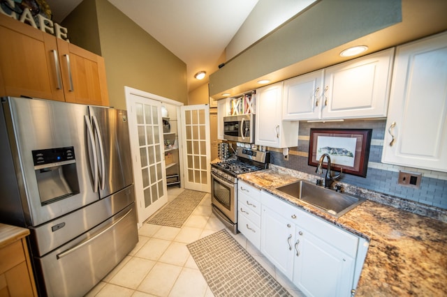 kitchen featuring light stone counters, stainless steel appliances, vaulted ceiling, sink, and white cabinetry