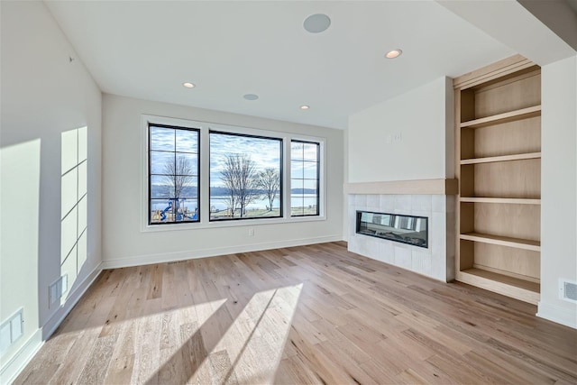 unfurnished living room featuring light hardwood / wood-style floors, built in features, and a tiled fireplace