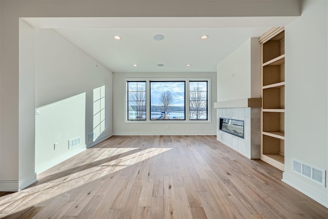 unfurnished living room featuring built in shelves, light hardwood / wood-style flooring, and a tiled fireplace