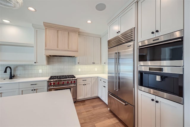 kitchen with backsplash, light hardwood / wood-style flooring, white cabinetry, and high quality appliances