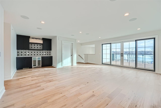 unfurnished living room featuring beverage cooler and light hardwood / wood-style floors