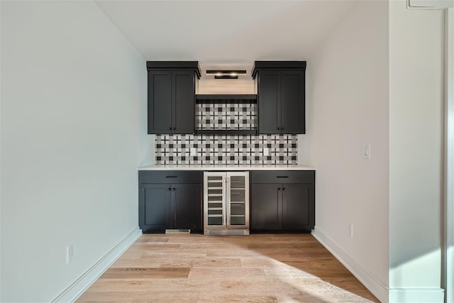 bar with decorative backsplash, light wood-type flooring, and beverage cooler