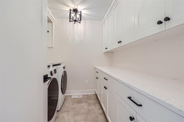 washroom with washing machine and clothes dryer, a chandelier, and cabinets