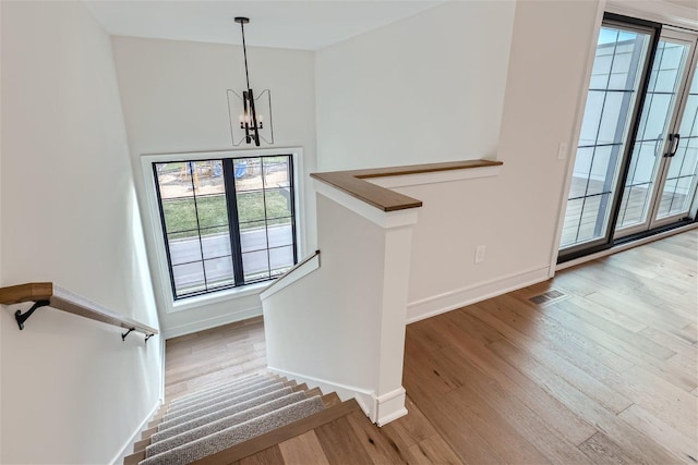 staircase featuring hardwood / wood-style flooring, a healthy amount of sunlight, and a notable chandelier