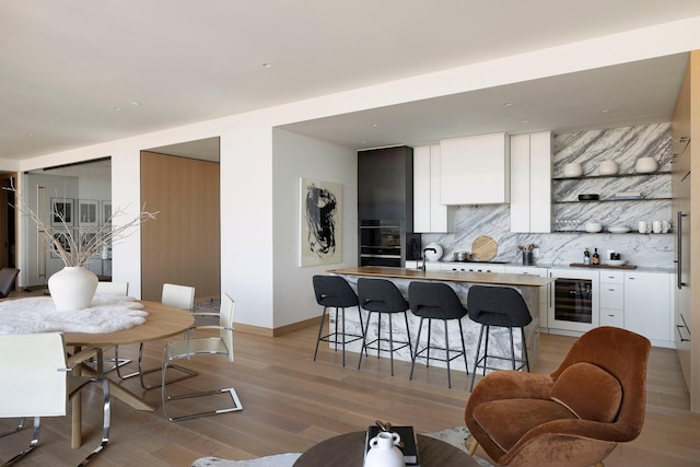 kitchen featuring backsplash, a kitchen bar, beverage cooler, white cabinetry, and light hardwood / wood-style floors