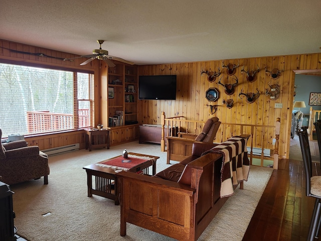 38257 Dove St, Spencer Twp, MN 56431 - carpeted living room featuring wooden walls, a ceiling fan, and a baseboard heating unit