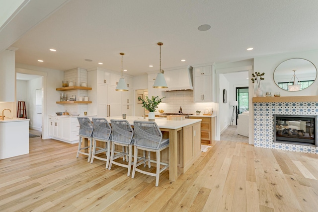 kitchen featuring white cabinets, custom range hood, light hardwood / wood-style floors, and a tile fireplace