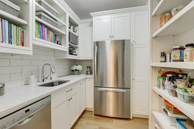 kitchen with tasteful backsplash, white cabinetry, stainless steel appliances, light wood-type flooring, and sink