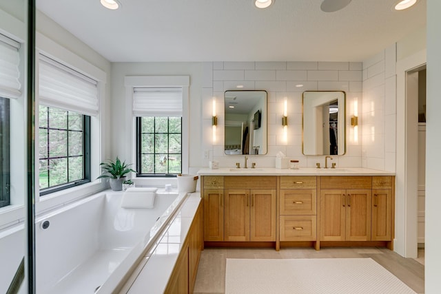 bathroom featuring tile walls, tiled tub, tile floors, and dual bowl vanity