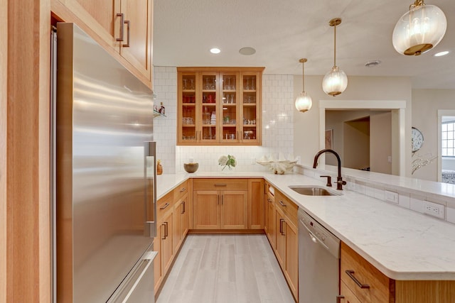 kitchen with light wood-type flooring, tasteful backsplash, stainless steel appliances, decorative light fixtures, and sink