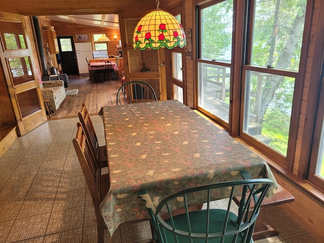 dining room with wooden walls, lofted ceiling, dark wood-type flooring, and a healthy amount of sunlight