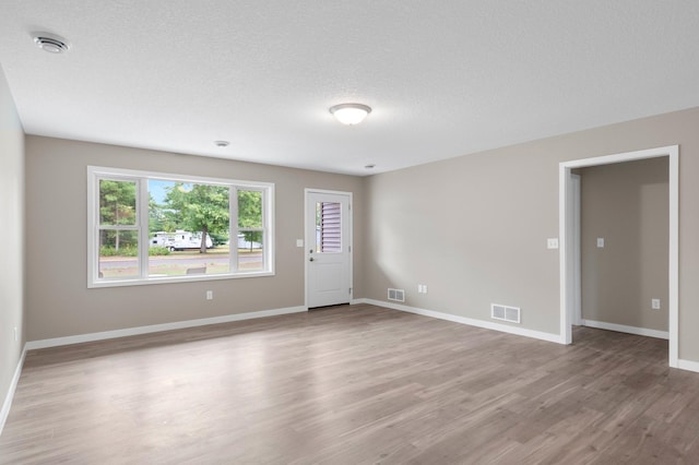 empty room with a textured ceiling and light hardwood / wood-style flooring