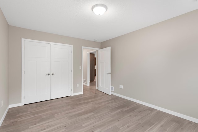 unfurnished bedroom with light wood-type flooring, a textured ceiling, and a closet