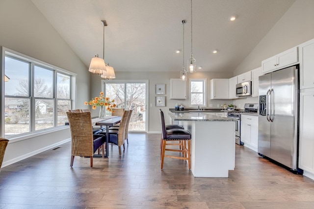 kitchen featuring white cabinets, decorative light fixtures, appliances with stainless steel finishes, and hardwood / wood-style flooring