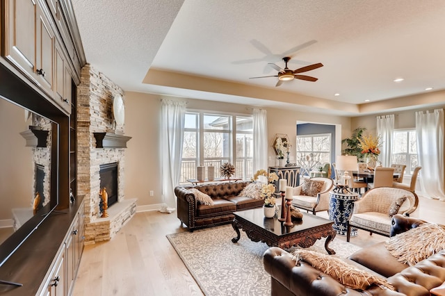 living room with light hardwood / wood-style floors, a textured ceiling, a fireplace, a raised ceiling, and ceiling fan