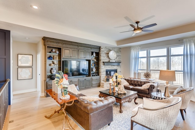 living room with ceiling fan, light hardwood / wood-style floors, and a stone fireplace