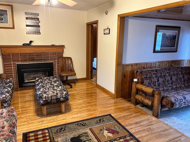 living room featuring a brick fireplace, hardwood / wood-style flooring, ceiling fan, and wooden walls