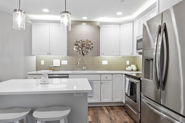 kitchen featuring dark wood-type flooring, white cabinets, sink, decorative light fixtures, and stainless steel appliances