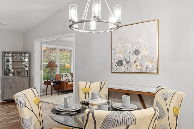 dining space with hardwood / wood-style flooring, a chandelier, and vaulted ceiling