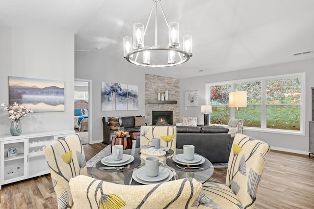 dining area featuring a fireplace, light wood-type flooring, lofted ceiling, and a notable chandelier