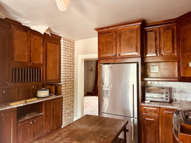 kitchen featuring brick wall, light stone counters, stove, tasteful backsplash, and stainless steel refrigerator