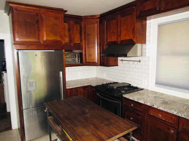 kitchen with light stone countertops, backsplash, light tile flooring, stainless steel fridge with ice dispenser, and black range with gas stovetop