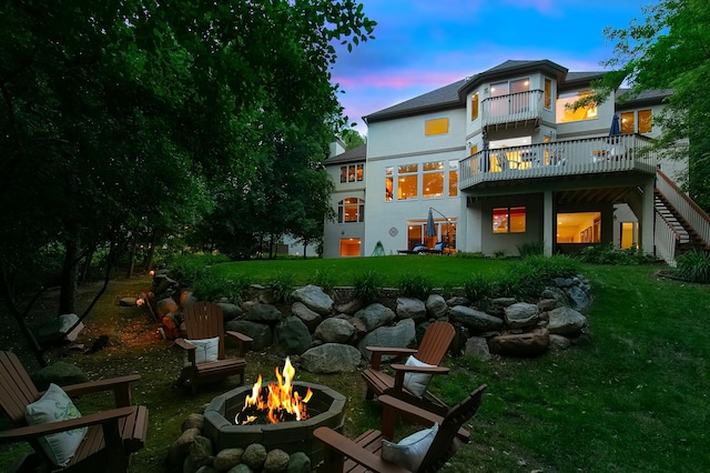 back house at dusk featuring an outdoor fire pit and a lawn