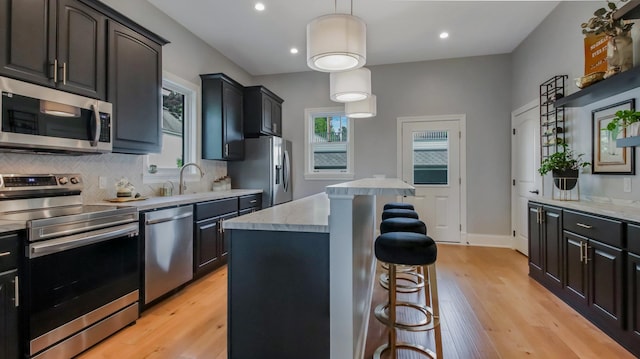 kitchen with stainless steel appliances, sink, decorative light fixtures, light hardwood / wood-style floors, and a kitchen island