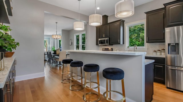 kitchen with appliances with stainless steel finishes, light wood-type flooring, decorative light fixtures, and a kitchen island