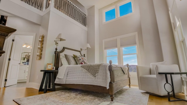 bedroom featuring connected bathroom, light hardwood / wood-style flooring, and a high ceiling