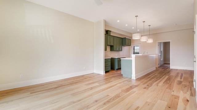 kitchen featuring tasteful backsplash, light wood-type flooring, decorative light fixtures, a center island with sink, and green cabinets