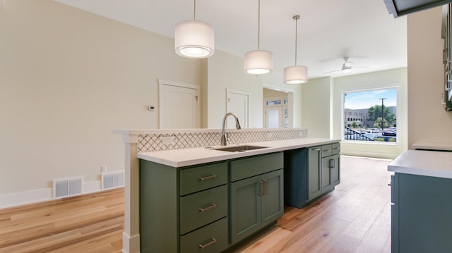 kitchen featuring green cabinetry, pendant lighting, light wood-type flooring, ceiling fan, and sink