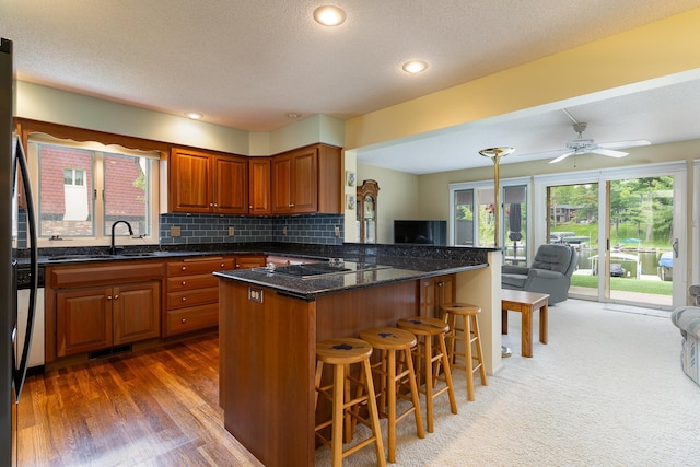 kitchen with dark wood-type flooring, kitchen peninsula, a kitchen bar, backsplash, and ceiling fan