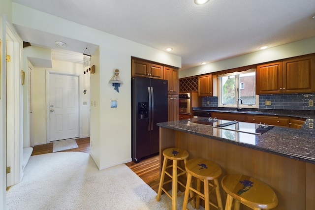 kitchen featuring tasteful backsplash, a breakfast bar, black appliances, wood-type flooring, and sink