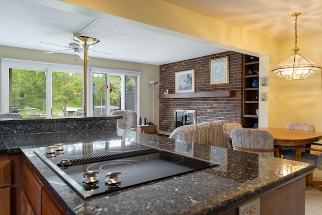 kitchen featuring pendant lighting, a textured ceiling, ceiling fan with notable chandelier, a brick fireplace, and black electric cooktop