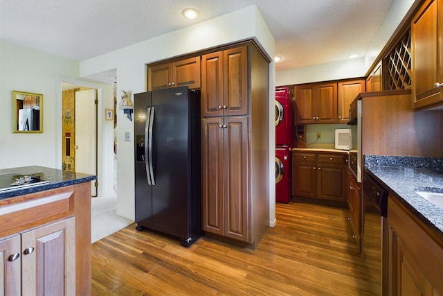 kitchen featuring stacked washer and clothes dryer, black dishwasher, dark stone counters, dark hardwood / wood-style floors, and stainless steel fridge with ice dispenser