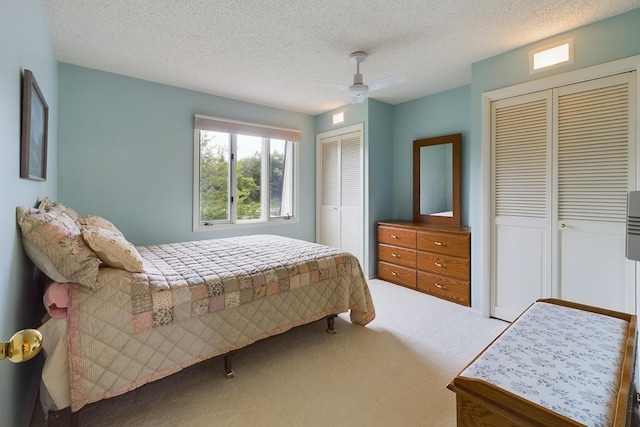 bedroom featuring ceiling fan, multiple closets, a textured ceiling, and carpet