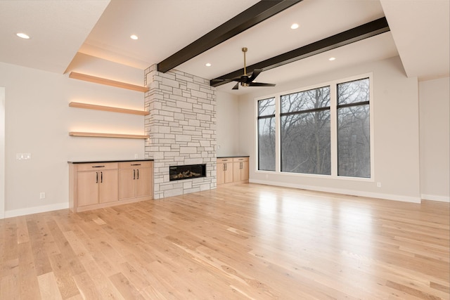 unfurnished living room with beamed ceiling, light wood-style flooring, a fireplace, and baseboards