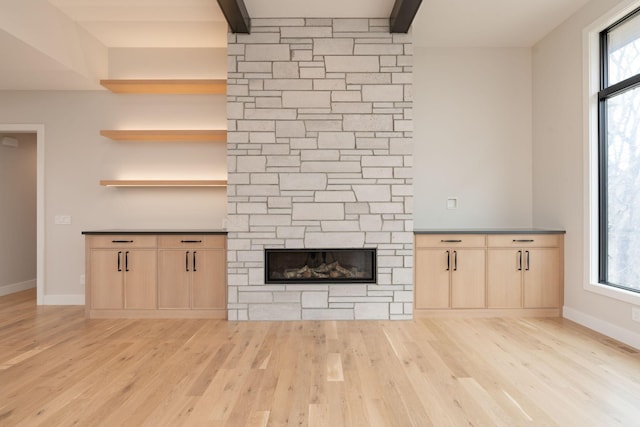 unfurnished living room with beamed ceiling, baseboards, a fireplace, and light wood finished floors