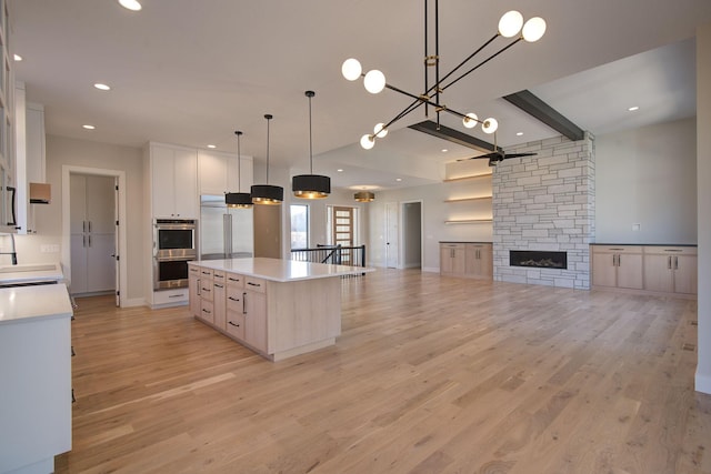 kitchen featuring light wood-type flooring, a stone fireplace, white cabinets, and appliances with stainless steel finishes