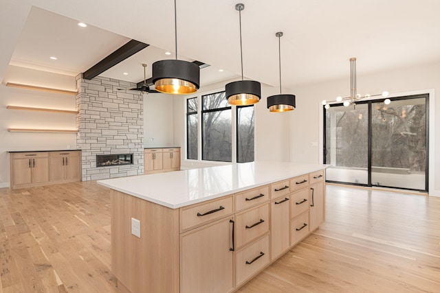 kitchen with light brown cabinets, a kitchen island, light countertops, light wood-style flooring, and a fireplace