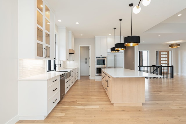 kitchen with light wood finished floors, a kitchen island, decorative backsplash, stainless steel appliances, and a sink