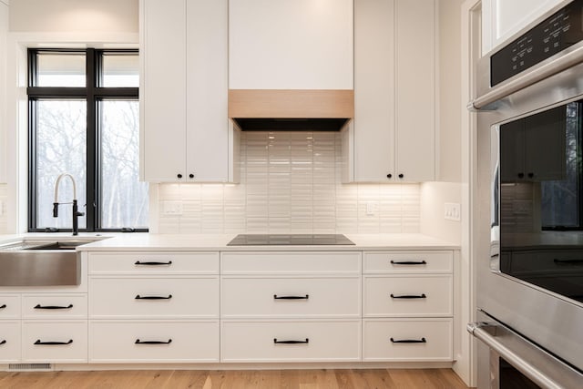 kitchen featuring a sink, black electric stovetop, backsplash, and white cabinetry