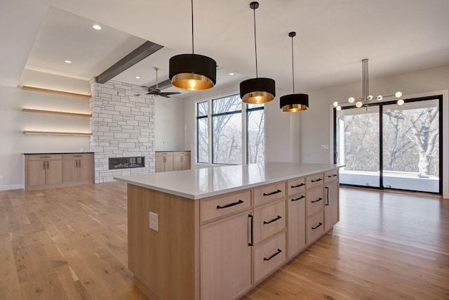 kitchen featuring open floor plan, light countertops, light wood-type flooring, a fireplace, and a ceiling fan