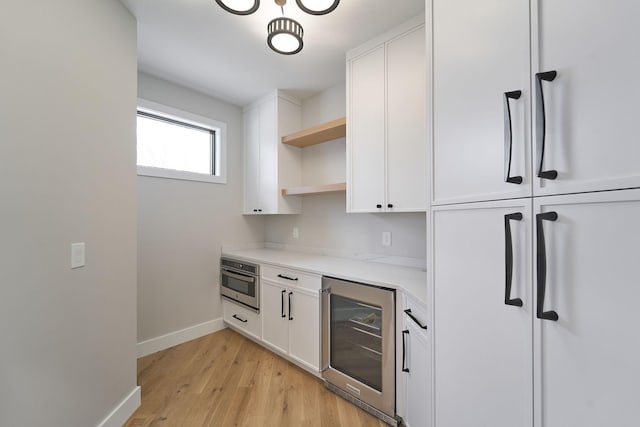 interior space with baseboards, beverage cooler, stainless steel oven, light wood-style flooring, and fridge