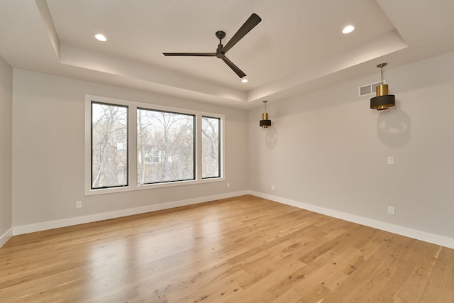 empty room featuring a raised ceiling, light wood-style flooring, and baseboards