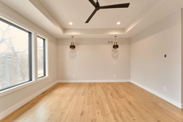 empty room featuring light wood finished floors, recessed lighting, baseboards, and a tray ceiling